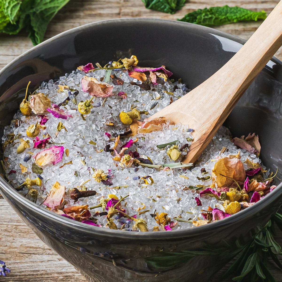 Black bowl filled with medium grain bath salt mixed with dried flowers and wooden scoop