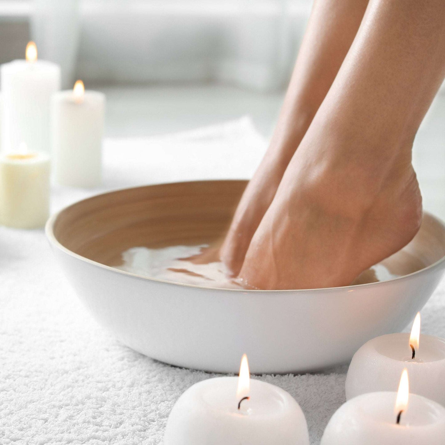 Feet soaking in wooden bowl with water surrounded by white lit candles for relaxing spa treatment with Ultra Epsom Unscented Bath Salt.